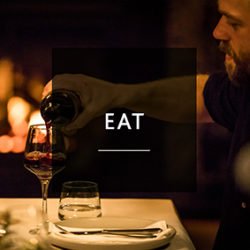 EAT man pouring wine fireplace background dark room